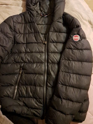 Svart Colmar pufferjacka med huva - Säljer en svart pufferjacka från Colmar Originals med huva och två dragkedjeförsedda fickor. Jackan har quiltad design och Colmar-logga på ärmen. Perfekt för kalla dagar och riktigt snygg till streetwear-stilen.