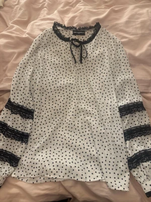 Karl Lagerfeld polkadot blus - Säljer min Karl Lagerfeld blus som jag köpte på Sellpy 2022. Inte använt själv men köpte den i använt skick, så det finns en väldigt liten fläck vid urringningen (som man knappt ser). Super söt prickig blus, svart spets vid ärmar och kragen, snörning vid kragen och knappar vid ärmarna. Super fin till kostymbyxor!🎀 Nypris 600 kr