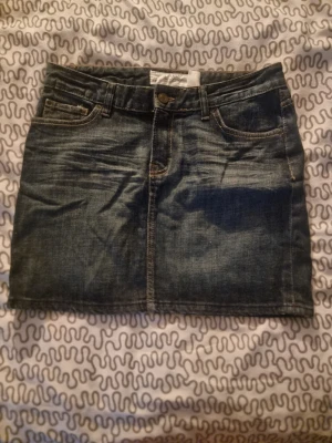 Mörkblå jeanskjol med fickor - Säljer en mörkblå jeanskjol från H&M i klassisk denimstil. Kjolen är kort och har både fram- och bakfickor samt hällor för bälte. Perfekt för dig som gillar en enkel och cool look. Passar till sneakers eller boots.