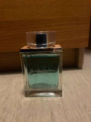 Baldessarini fräsch parfymflaska - Snygg parfym från Baldessarini med blågrön vätska och kompassdesign på flaskan. Volymen är 90 ml. Perfekt för dig som vill sticka ut med en modern och stilren doft. Tillverkad i Tyskland.