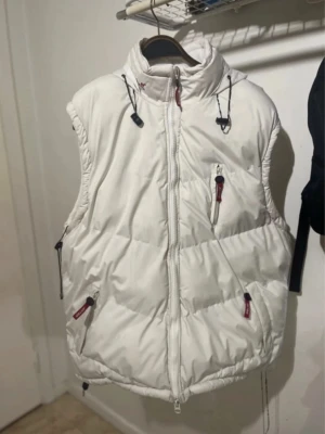 Fodrad väst  - Vit fodrad väst från Sportswear i storleken L med dragkedja och tre fickor framtill. Västen har dessutom två andra fickor på insidan och är perfekt om man vill ha det lite varmare.  Färgen är mer crème på utsidan och vit på insidan.