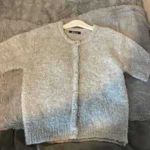 Grå kofta från Gina Tricot XS - Supermjuk och fluffig grå kofta från Gina Tricot i storlek XS. Koftan har korta ärmar, rund halsringning och knäpps med silvriga knappar framtill. Aldrig använd 