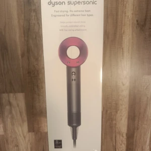 Dyson Supersonic hårfön med tillbehör - Dyson Supersonic hårfön i metallicgrå och rosa med fem stylingmunstycken. Ergonomisk design med rund öppning och magnetiska tillbehör för olika hårtyper. Perfekt för att skapa snygga frisyrer snabbt utan extrem värme. Levereras i originalförpackning med sladd.
