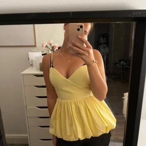 Gul omlott linnetopp med volang - Superfin gul linnetopp med omlott framtill och bred volang nedtill. Toppen har smala justerbara axelband och smockad rygg för extra komfort. Perfekt för sommarens alla tillfällen och ger en söt och trendig look.