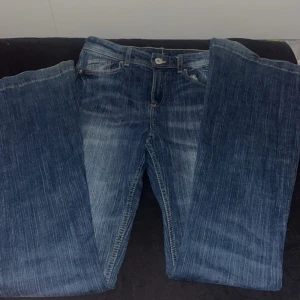 Blå flared jeans från H&M, mid waist - Snygga blå jeans från H&M med flared ben och justerbar midja. Jeansen har en klassisk tvättad look och mid waist-passform. Perfekta för dig som gillar en trendig och bekväm stil.