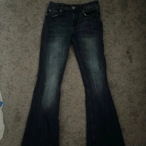 Mörkblå bootcut jeans - Snygga mörkblå bootcut jeans med en klassisk femficksdesign. Jeansen har en lätt tvättad look och är perfekta för en avslappnad stil. De har en knapp och dragkedja framtill.