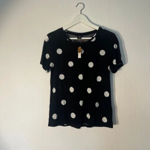 Svart prickig t-shirt från Lindex - Svart t-shirt från Lindex med stora vita prickar över hela plagget. Rund halsringning och korta ärmar. Mjuk och skön bomullskvalitet som känns chill och enkel att matcha med jeans eller shorts. Ny med prislapp!