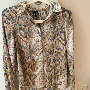 Ormmönstrad skjorta från Zara  - Snygg skjorta från Zara  med ormmönster i beige, brunt och svart. Skjortan har klassisk krage, knappar framtill och långa ärmar. Perfekt för dig som vill sticka ut med ett djurmönster och gillar trendiga detaljer.