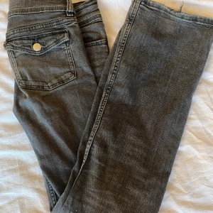 Grå jeans från Gina Tricot, stl 146 - Snygga grå lågmidjade jeans från Gina Tricot i storlek 146. Jeansen har klassisk femficksdesign, dubbla knappar i midjan och utsvängdaben. Materialet är mjukt denim och färgen är tvättad grå med lite slitningar för en cool look. Lite fläckar.