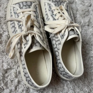 Guess sneakers med monogrammönster - Snygga sneakers från Guess med grått och vitt monogrammönster. Skorna har rund tå, snörning och är tillverkade i textil med vita detaljer. Perfekta för dig som gillar stilrena och trendiga skor med logga. Använda 2 gånger! 