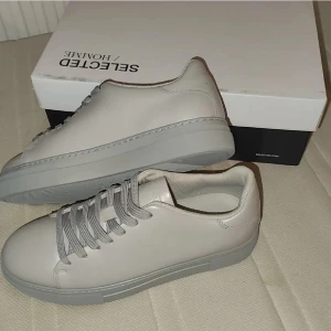 Chunky grå sneakers från Selected Homme - Chunky sneakers i ljusgrått skinn från Selected Homme. Snygg minimalistisk design med matchande grå snörning och platt sula. Perfekta för dig som gillar cleana och stilrena skor med modern vibe.