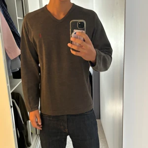 Mörkgrå v-ringad tröja Marlboro Classics - Säljer en mörkgrå v-ringad tröja från Marlboro Classics i bomull. Tröjan har lång ärm, diskret logga broderad på bröstet och en klassisk, stilren look. Perfekt för dig som gillar enkel och snygg stil.