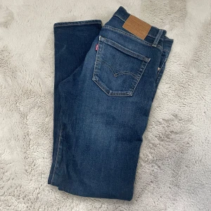 Levi's 511 blå jeans med slitningar - Säljer ett par Levi's 511 jeans i mörkblå tvätt med snygga slitningar och distressed detaljer. Modellen är slim och sitter tajt över benen. Klassisk femficksdesign, tillverkade i bomull med lite stretch för skön passform. Perfekta för dig som gillar en modern och avslappnad look.