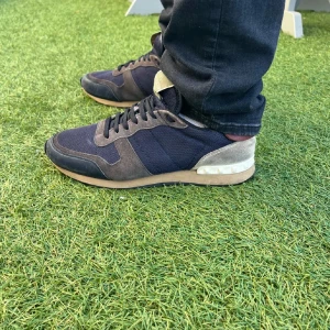 Valentino Rockrunner sneakers blå/grå - Snygga Valentino Rockrunner sneakers i mörkblå mesh och grå mocka med detaljer i beige och vinrött. Skorna har klassisk snörning, platt sula och rund tå. Perfekta för dig som vill ha en exklusiv och sportig look med lyxig känsla.