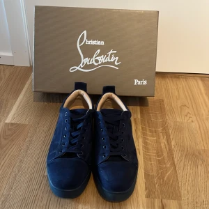 Mörkblå Louboutins | 39,5 - Snygga mörkblå sneakers från Christian Louboutin i lyxig mocka med klassisk röd sula och diskret broderad logga på hälen. Skorna har svarta snören, rund tå och mjuk beige insida. Perfekta för dig som vill sticka ut med exklusiv stil. Tvättar skorna innan om det skulle viljas😃