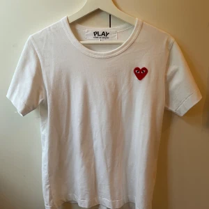 Vit Comme des Garçons Play t-shirt  - Vit t-shirt från Comme des Garçons Play i bomull med klassisk passform. På bröstet sitter det ikoniska röda hjärtat med ögon, broderat. Strorleken är S men skulle säga att den passar XS också då de är små i storlekarna. Priset är inte hugget i sten. Har du frågor eller funderingar bara hör av dig så svarar jag gärna!!