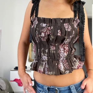 korsettopp med volang  - Supersöt brun korsettopp med blommigt mönster i rosa och lila toner. Toppen smockad struktur som ger en snygg passform. Från h&m’s kollektion med Brock collection 