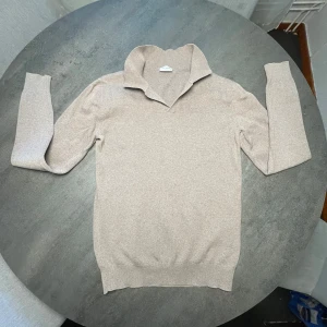 Beige stickad tröja från John Henric - Säljer en stilren beige stickad tröja från John Henric. Tröjan har en klassisk krage med v-ringning och ribbade muddar vid ärmslut och nederkant. Perfekt för lager-på-lager och passar till många olika outfits.