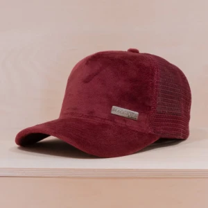 Vinröd keps i sammet från Maggiore - Snygg vinröd keps från Maggiore i mjuk sammet med mesh på sidorna och bak. Kepsen har böjd skärm och en metallbricka med logga framtill. Perfekt accessoar för en cool och avslappnad stil.