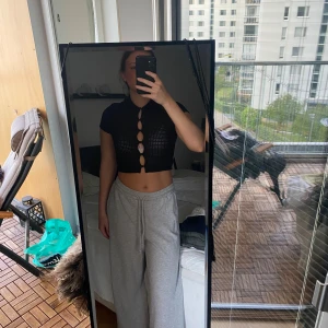 Svart croppad topp från H&M Divided - Svart croppad topp från H&M Divided med korta ärmar och krage. Toppen har ett coolt hålmönster och flera runda öppningar framtill som hålls ihop med små knytdetaljer. Perfekt för dig som vill sticka ut med en edgy stil.