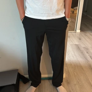 Svarta kostymbyxor från Jack & Jones - Svarta kostymbyxor från Jack & Jones med relaxed fit. Byxorna har raka ben, sidofickor och knappar bak. Perfekta för en clean och stilren look. Materialet känns mjukt och följsamt, vilket gör dem riktigt sköna att bära. Waist:30 Längd:34