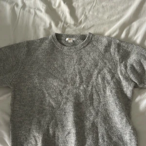 Grå stickad tröja från Gina Tricot - Mysig grå stickad tröja från Gina Tricot med rund halsringning och ribbade muddar. Enkel och stilren design som funkar till det mesta. Passar dig som gillar en klassisk look.
