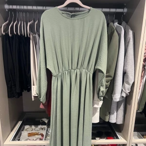 Långklänning med resårmidja - Snygg ljusgrön långklänning med rund hals och långa ärmar. Klänningen har en markerad midja med resår som ger en skön passform och ett flowy fall. Materialet är mjukt och lätt, perfekt för vår och sommar. Enkel och stilren design som är lätt att matcha. Strl S/M