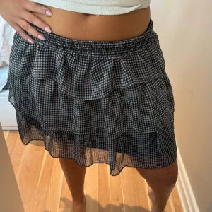 Rutig volangkjol från H&M Divided - Supersöt kort volangkjol från H&M Divided i svartvitt rutigt mönster. Kjolen har flera lager med volanger och resår i midjan för en bekväm passform. Tillverkad i tunn, luftig polyester som ger en lätt känsla.