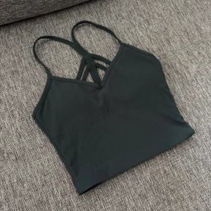 Mörkgrön ribbad topp Aim'n XS - Säljer en mörkgrön ribbad linnetopp från Aim'n i storlek XS. Toppen har smala axelband som korsas i ryggen och en snygg v-ringning framtill. Perfekt för träning eller chill dagar. Materialet är stretchigt och följsamt för bästa komfort.