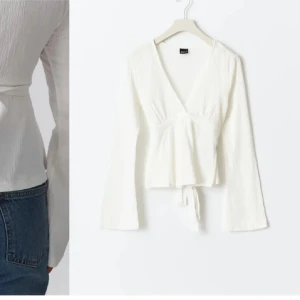 Vit omlottopp med knytband - Säljer en vit omlottopp från Gina med v-ringning och långa ärmar. Toppen har knytband i midjan som ger en snygg siluett och är tillverkad i ett lätt, strukturerat tyg. Perfekt att styla med jeans eller kjol för en fräsch look.