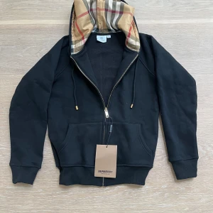Svart hoodie från Burberry med mönstrad huva - Riktigt fet svart burberry hoodie i storlek S men passar cirka 160-168! Inga tydliga defekter och bra pris! Har ni frågor är det bara fråga!