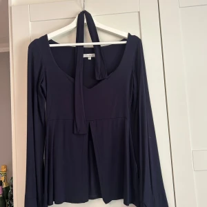 Svart långärmad topp med knyt - Supersnygg svart långärmad topp från Design by Si med djup v-ringning och knyt framtill. Modellen har lätt utsvängda ärmar o snöret går att ta bort. Passar allt från S till L så tyget är stretchigt