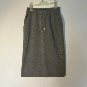 Grå långkjol med snörning XS - Superskön grå långkjol i storlek XS från Lindex med elastisk midja och snörning framtill. Kjolen har praktiska fickor på sidorna och är gjord i mjukt bomullsmaterial. Ny med prislapp