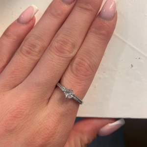 Silverring med glittrande sten - Snygg silverfärgad ring med en gnistrande rund sten i mitten och små stenar längs bandet. Perfekt för dig som gillar stilrena och eleganta smycken med lite extra bling. Passar både till vardags och när du vill känna dig extra fin.