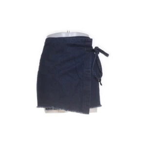 Mörkblå omlottjeanskjol BDG - Snygg mörkblå kort jeanskjol från BDG Urban Outfitters i omlottmodell med knytband i sidan. Kjolen passar perfekt till sneakers eller boots. Modellen är enkel och stilren, vilket gör den lätt att matcha.