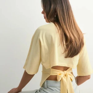 Gul omlottopp med knyt i ryggen - säljer denna gula t shirt från nelly då den inte används längre, väldigt bra skick då den inte är använd så mycket. skriv för fler bilder💓