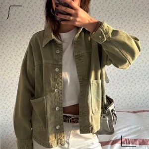 Olivgrön jeansjacka från Zara - Säljer en olivgrön jeansjacka från Zara med klassisk krage, stora fickor framtill och knäppning med silvriga knappar. Jackan har en loose passform och är tillverkad i kraftigt bomullstyg. Perfekt att slänga över en t-shirt för en chill look.