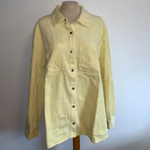 Gul skjorta från H&M - Ljusgul skjorta från H&M med klassisk krage, tryckknappar och två stora bröstfickor. Skjortan har lång ärm och en loose passform som ger en chill vibe. 