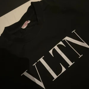 Svart VLTN t-shirt från Valentino - Svart t-shirt från Valentino med stor vit VLTN-logga på bröstet. Klassisk rund hals och korta ärmar. T-shirten har en clean och stilren look, perfekt för dig som gillar designerplagg med tydlig branding. Materialet känns mjukt och skönt mot huden.