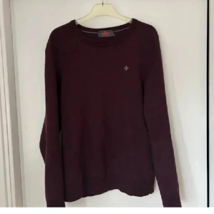 Mörkröd stickad tröja från Morris - Snygg mörkröd stickad tröja från Morris med rund halsringning och diskret logga på bröstet. Långärmad modell i mjukt material som passar perfekt till jeans eller chinos. Enkel och stilren design som funkar året runt.