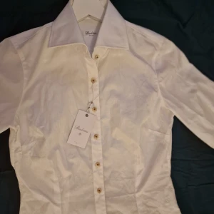 Vit skjorta från Stenströms - Klassisk vit skjorta från Stenströms i slimline-modell. Skjortan är tillverkad i 100% bomull, har snygga pärlemorknappar och broderad logga vid nederkanten. Perfekt för en clean och stilren look. Nypris 1100 kr.