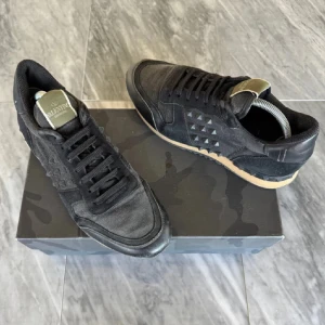 Valentino Garavani rockrunners  - Svarta Valentino Garavani sneakers med ikoniska nitar på sidorna. Skorna har snörning, rund tå och en kontrasterande beige sula. Materialmix av mocka och textil ger en lyxig känsla. Perfekta för dig som vill ha en edgy och exklusiv look.