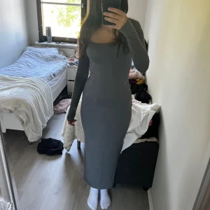Grå långärmad tight maxiklänning - Säljer en stilren grå långklänning med lång ärm och figurnära passform. Klänningen har en snygg, något offshoulder urringning och är tillverkad i ett stretchigt material som sitter riktigt snyggt på kroppen. Perfekt för dig som gillar minimalistisk och clean stil.