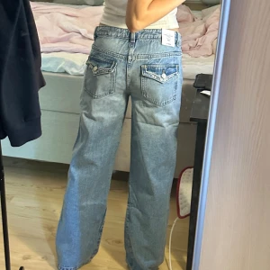 Ljusblå paljettjeans från Gina Tricot - Säljer ett par helt nya ljusblå jeans från Gina Tricot med låg midja och raka, lite loose ben. Bakfickorna har snygga detaljer med paljetter och broderier som ger extra bling. Klassisk jeanslook med knapp och dragkedja framtill. Perfekta för dig som vill sticka ut lite extra. Lapparna kvar för bara testade, storlek 164 vilket passar en XS/34, köpte för 400kr