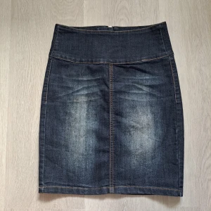 Mörkblå jeanskjol från Pieces - Snygg mörkblå jeanskjol från Pieces med hög midja och klassiska fickor bak. Kjolen har en rak, kort passform och dragkedja bak. Perfekt för dig som gillar en enkel men cool denimstil.
