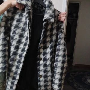 Rutig ullkappa från MNG Collection - Säljer en snygg rutig kappa från MNG Collection i storlek M. Jackan har svart och vit mönster, klassisk krage och knäppning med knappar framtill. Materialet är mjuk ull och kappan har långärmade ärmar. Perfekt för dig som gillar statement-plagg med retrovibe. Den kommer under rumpan🙃