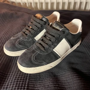 Valentino flycrews svarta  - Svarta och vita Valentino Garavani flycrew sneakers med snygg kontrastpanel i vitt på sidan. Skorna har rund tå, platt sula och svart snörning. Ovandelen är i mocka och skinn, med lyxig känsla och klassisk design. Perfekta för dig som gillar stilrena och exklusiva sneakers.