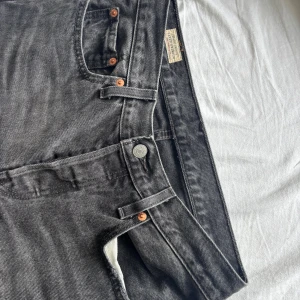 Levi's 501 grå jeans straight fit - Snygga grå Levi's 501 jeans i klassisk straight fit. Jeansen är tillverkade i robust denim och har fem fickor, knappgylf och den ikoniska läderpatchen bak. Perfekta för dig som gillar en tidlös look med en cool vintagekänsla.