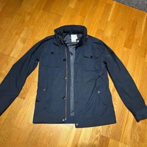 Marinblå vindjacka från J.Lindeberg - Tvär fet field jacka från J.Lindeberg.                   Storlek M jackan är i väldigt fint skick nästan som ny hör av er vid vid fler frågor/TTT