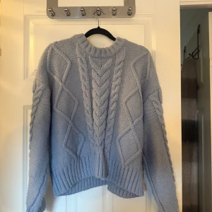 Ljusblå stickad kabeltröja - Supermysig ljusblå stickad tröja med grova kabelstickade detaljer och ribbade muddar. Tröjan har en klassisk rund halsringning och långa ärmar. Perfekt för kyliga dagar när du vill vara både varm och snygg.